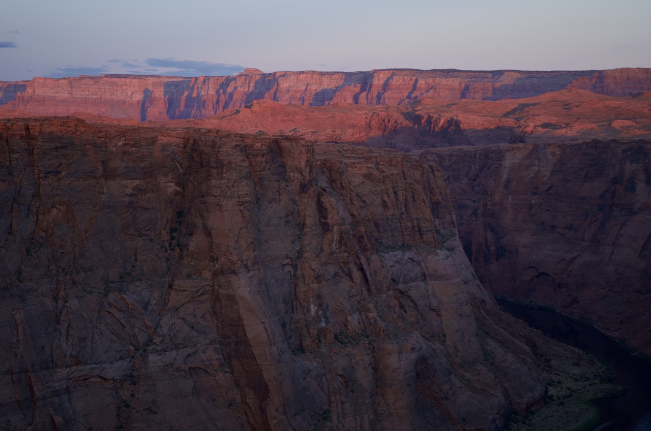 The sun begins to illuminate the mountains near Horseshoe Bend.